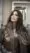 A woman with long, wavy brown hair and blonde highlights poses indoors in a textured brown jacket, touching her hair and gazing confidently to the side—capturing the perfect look from a top beauty salon.