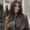 A woman with long, wavy brown hair and blonde highlights stands near a mirror in a modern, well-lit room—a chic look crafted by skilled hair stylists near me at a top beauty salon.