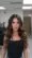A woman with long, wavy brown hair styled to perfection stands indoors in a black sleeveless top and gold necklaces—showcasing the expertise you’ll find at a beauty salon or with top hair stylists near me.